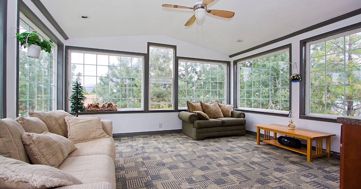White and grey sunroom with beige couch and ceiling fan with light